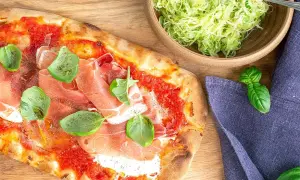 Pizza med prosciutto och basilika, perfekt till ett burrata recept. Bredvid en skål med krispig sallad.
