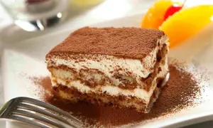 En bit krämig italiensk dessert, tiramisu, pudrad med kakao. Garnerad med apelsin och körsbär.