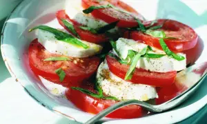 En Caprese-sallad med skivade tomater och mozzarella liknande ost, garnerad med färsk basilika och peppar.
