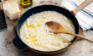 Krämig italiensk risotto i en panna, med en träsked som rör om. Parmesan och olivolja syns i bakgrunden.
