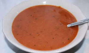 En skål med värmande linssoppa, perfekt för ett enkelt linssoppa recept. En sked vilar i den mustiga, röda soppan.