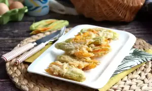 Friterad zucchini blomma serveras på en vit tallrik. Bredvid ligger en kniv och gaffel.