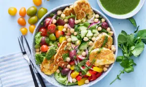 En härlig halloumi sallad med kikärtor, tomater, gurka, paprika och oliver, toppad med en grön dressing.