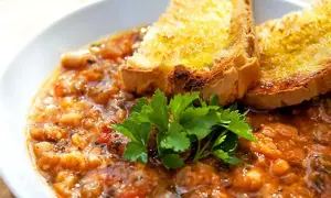 En mustig gryta med bönor och tomater, toppad med rostat bröd och persilja. Perfekt för ett enkelt svartkål recept.