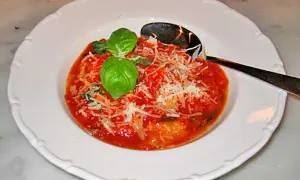 En portion pappa al pomodoro, en mustig tomatsoppa med bröd, toppad med basilika och parmesan. En sked ligger i skålen.