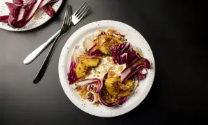 En tallrik med grillad persika, krämig burrata, krispig radicchio och örter. En utsökt sommarrätt.