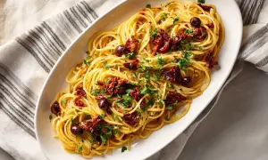En skål med spaghetti puttanesca, toppad med soltorkade tomater, oliver och persilja.