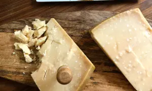 Två bitar Grana Padano parmesanost på en träskärbräda. En bit är uppbruten i mindre bitar.