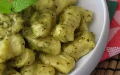 En skål med krämiga gnocchi pasta med pesto och en myntakvist.
