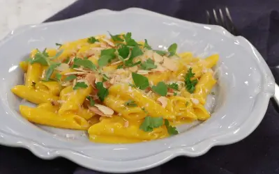 En krämig pasta milanese med mandelspån och färska örter, serverad i en ljusblå skål.