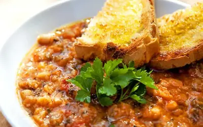 En mustig gryta med bönor och tomater, toppad med rostat bröd och persilja. Perfekt för ett enkelt svartkål recept.
