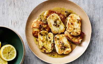 Stekt, marinerad halloumi med en kryddig dressing och chiliflakes. Serveras på en tallrik med citronklyftor vid sidan.