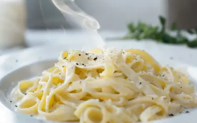 En ångande portion pasta alfredo, generöst toppad med riven parmesan och svartpeppar. Enkel men lyxig.