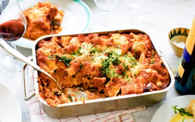En nybakad vegetarisk lasagne i formen, toppad med ost och persilja. Ett glas rödvin står bredvid.