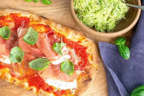 Pizza med prosciutto och basilika, perfekt till ett burrata recept. Bredvid en skål med krispig sallad.
