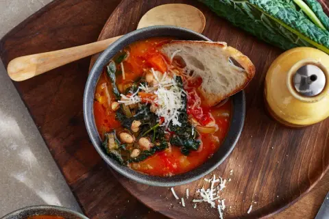 En skål med mustig italiensk soppa med bönor, grönsaker och en brödskiva, toppad med riven ost.