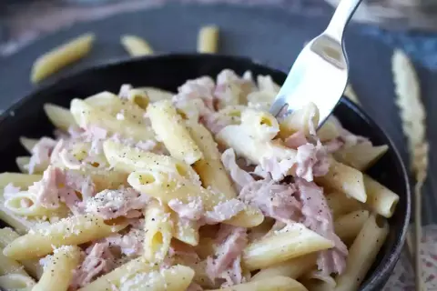 En gaffel lyfter en tugga av krämig skinksås pasta, toppad med riven ost och svartpeppar.