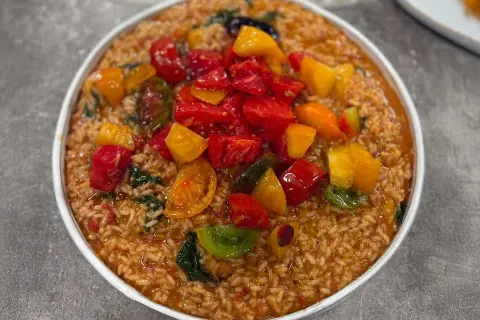 En skål med krämig risotto tomat, toppad med färgglada, saftiga tomater och gröna blad. En härlig sommarrätt.