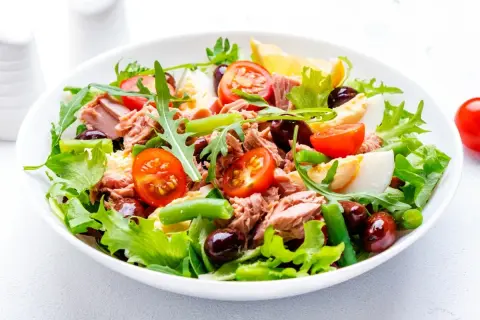 En fräsch sallad nicoise med tonfisk, ägg, tomater, oliver och gröna bönor på en bädd av sallad.
