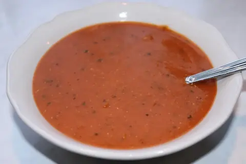 En skål med värmande linssoppa, perfekt för ett enkelt linssoppa recept. En sked vilar i den mustiga, röda soppan.