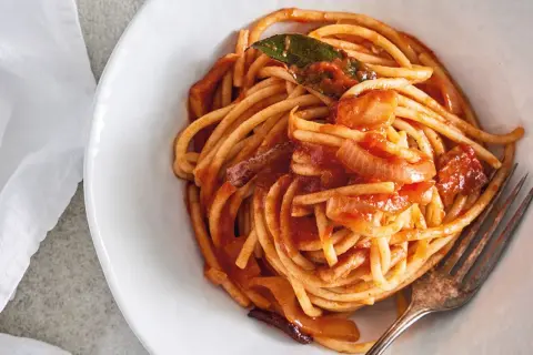 En skål med bucatini all'amatriciana, en klassisk italiensk pastarätt med tomatsås, lök och en lagerblad.