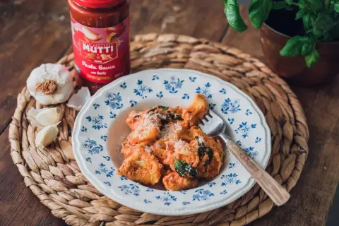 En tallrik med pasta i krämig tomatsås, toppad med parmesan. Bredvid står en burk Mutti pastasås och färsk vitlök. En perfekt italiensk meny fest!