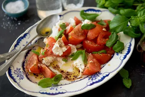 En härlig caprese sallad med saftiga tomater, krämig mozzarella och färsk basilika, ringlad med olivolja och balsamvinäger.