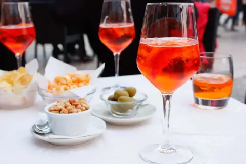 En aperitivo betyder njutning före maten. Här syns Aperol Spritz med snacks som nötter, oliver och chips.
