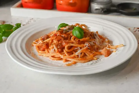 En tallrik med bucatini pasta i tomatsås, toppad med riven parmesan och färsk basilika. Ett perfekt bucatini pasta recept för en god middag.