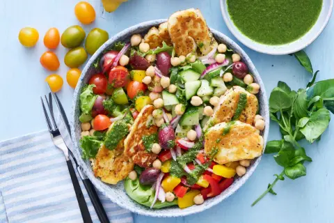En härlig halloumi sallad med kikärtor, tomater, gurka, paprika och oliver, toppad med en grön dressing.