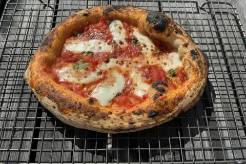 En perfekt napolitansk pizza, nybakad i ugnen, vilar på ett galler. Den har en bubblig, lätt bränd kant och är täckt av tomatsås och smält mozzarella.