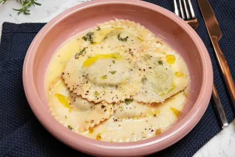 En skål med krämig ravioli, perfekt för ett enkelt ravioli recept. Garnerad med örter och parmesan.