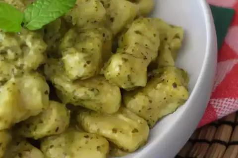 En skål med krämiga gnocchi pasta med pesto och en myntakvist.