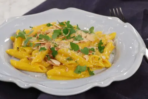 En krämig pasta milanese med mandelspån och färska örter, serverad i en ljusblå skål.