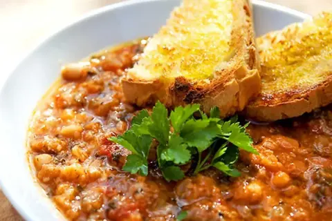 En mustig gryta med bönor och tomater, toppad med rostat bröd och persilja. Perfekt för ett enkelt svartkål recept.