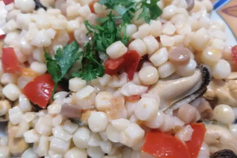 En närbild på en tallrik med fregola pasta, musslor och tärnad tomat, toppad med färsk persilja.