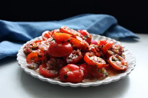 En härlig tomat sallad med rödlök och örter, serverad på en vit, mönstrad tallrik.