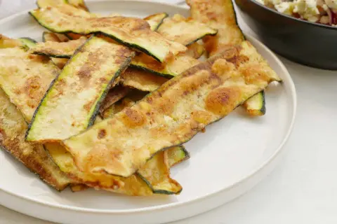 Krispiga, gyllene skivor av friterad zucchini ligger staplade på en vit tallrik, redo att avnjutas som ett lätt tilltugg.