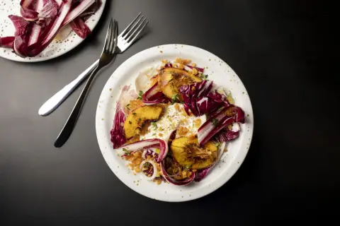 En tallrik med grillad persika, krämig burrata, krispig radicchio och örter. En utsökt sommarrätt.