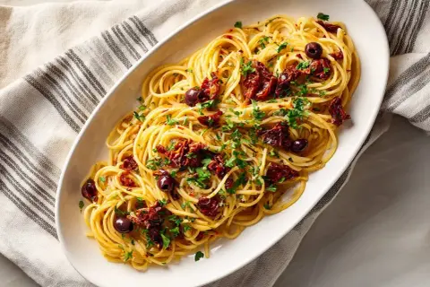 En skål med spaghetti puttanesca, toppad med soltorkade tomater, oliver och persilja.