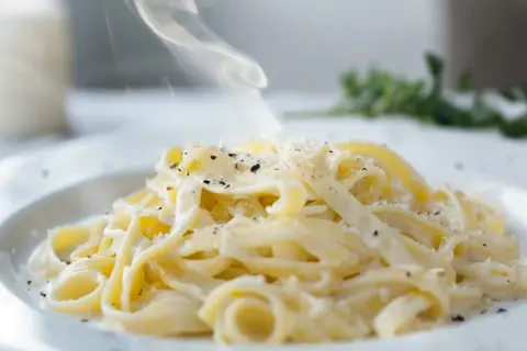 En ångande portion pasta alfredo, generöst toppad med riven parmesan och svartpeppar. Enkel men lyxig.