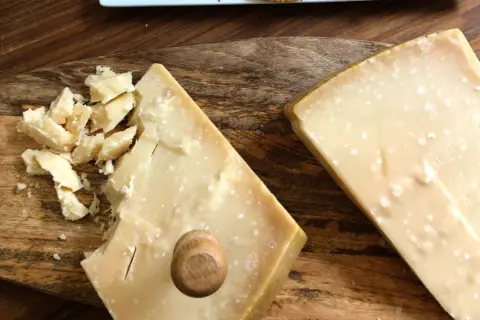 Två bitar Grana Padano parmesanost på en träskärbräda. En bit är uppbruten i mindre bitar.