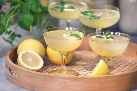 Fyra glas med gyllene limoncello, garnerade med citron och mynta. Perfekt för att lära sig hur dricker man limoncello en varm sommardag.