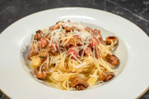 En tallrik med pasta alla boscaiola, toppad med riven parmesan och champinjoner.