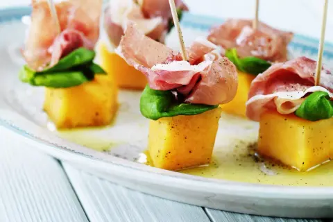 Melonbitar med prosciutto och basilika på ett fat. En klassisk och läcker kombination.