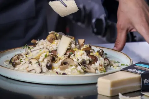 Krämig risotto svamp toppas med hyvlad ost. En vegansk ostbit ligger bredvid.
