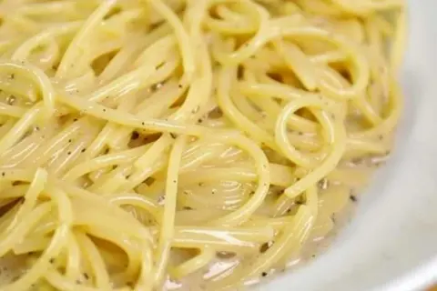 En närbild på en krämig portion spaghetti cacio e pepe, med synliga pepparkorn i den lena såsen.
