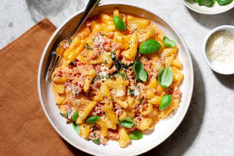 En skål med pasta alla norcina, krämig och toppad med färsk basilika och riven parmesan.