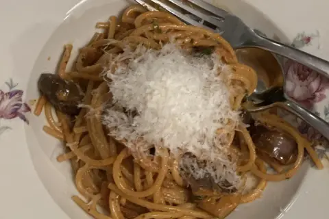 En tallrik med pasta alla norma, toppad med riven ost. Auberginebitar syns bland spaghettin.
