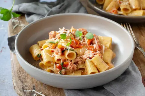 En skål med rigatoni pasta med salsicciapasta recept, toppad med riven parmesan och färsk basilika.